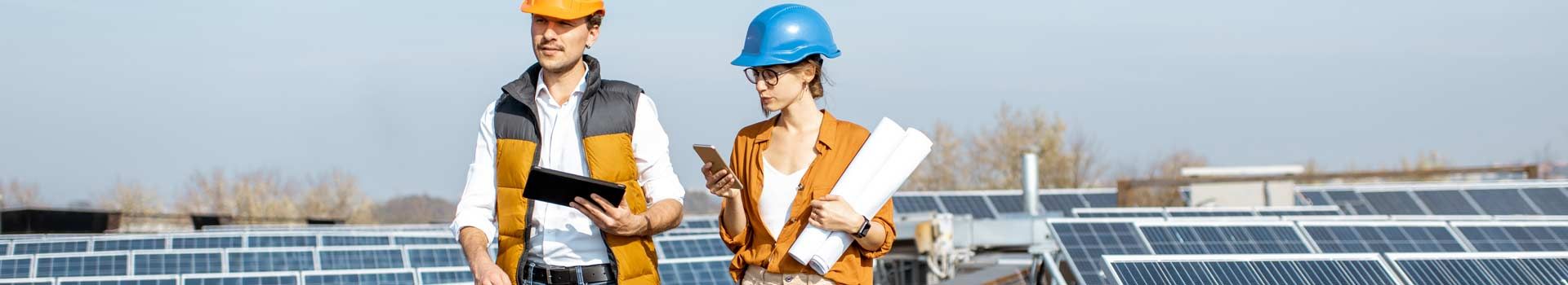 Zwei Personen mit Schutzhelmen und Planungsunterlagen vor Solarmodulen