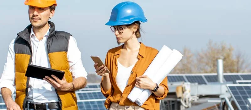 Zwei Personen mit Schutzhelmen und Planungsunterlagen vor Solarmodulen