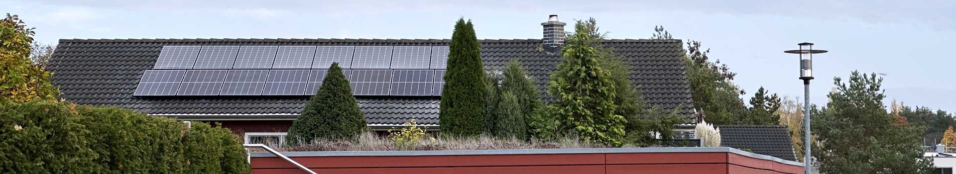 Solarmodule auf dem Dach eines Wohnhauses hinter Bäumen