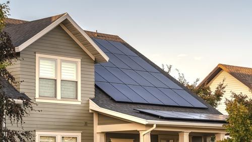 Haus mit Solarmodulen auf einer geneigten Dachfläche neben einer Gaube
