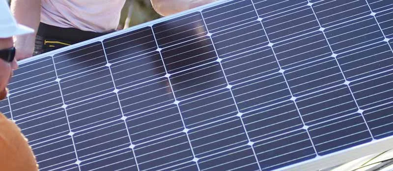 Monteure tragen ein Solarmodul auf einem Dach