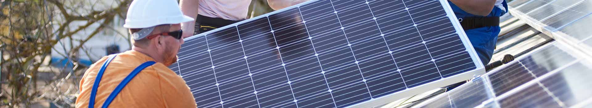 Monteure tragen ein Solarmodul auf einem Dach