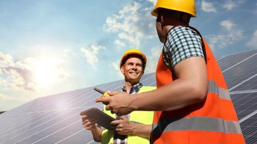 Zwei Personen mit Schutzhelmen und Tablet vor Solarmodulen
