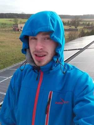 Monteur in Arbeitsjacke auf einem Dach, dahinter eine fertig belegte Modulfläche