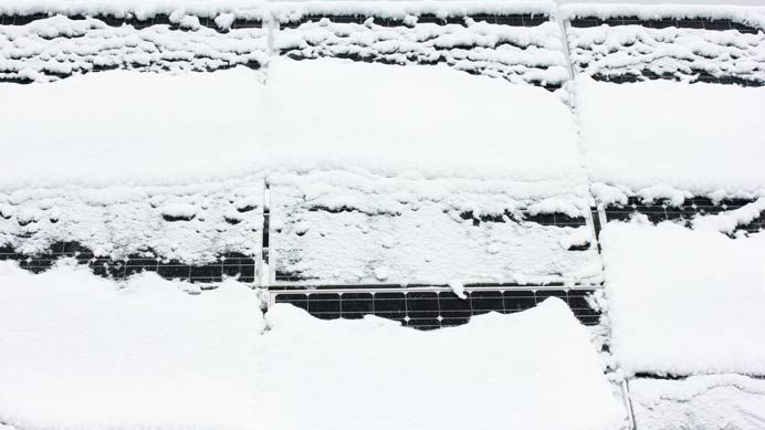 Weitgehend schneebedeckte Solarmodule mit schmalen freien Bereichen