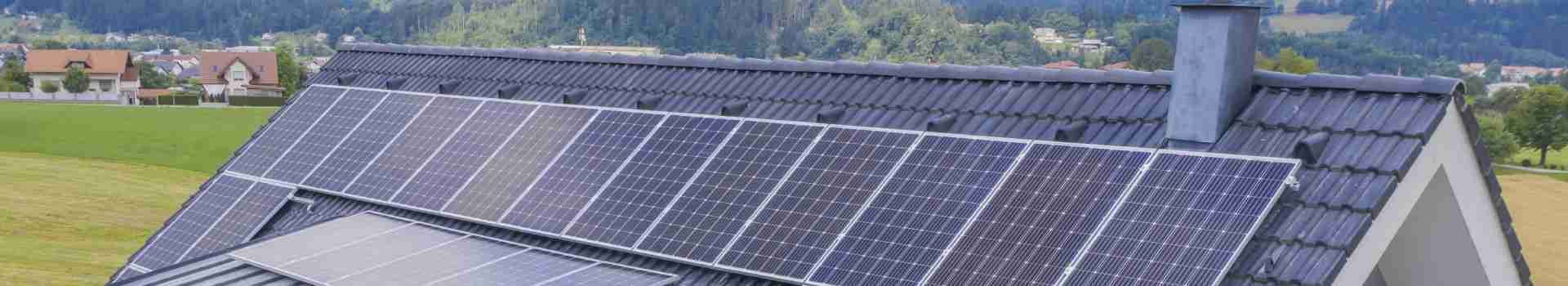Photovoltaik-Anlage auf einem geneigten Hausdach vor Wiesen und Wald