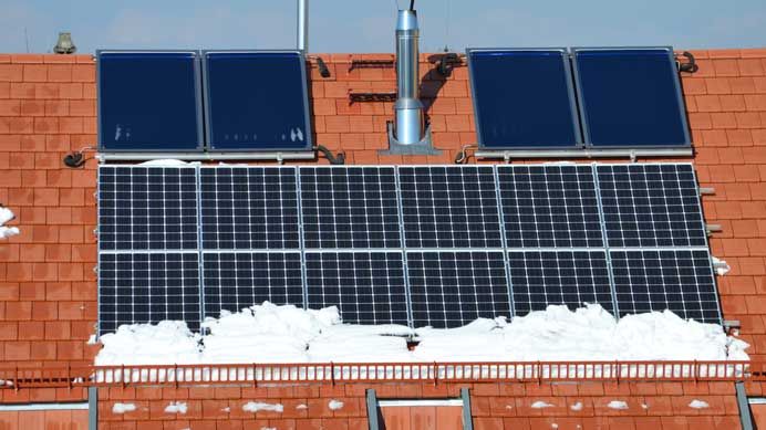 Photovoltaikmodule und darüber montierte Solarthermiekollektoren auf einem teilweise verschneiten Dach