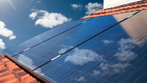 Solarmodule auf rotem Ziegeldach mit Spiegelungen von Wolken