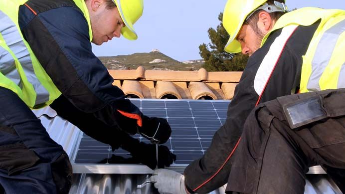 Zwei Handwerker arbeiten an Solarmodulen auf einem Dach