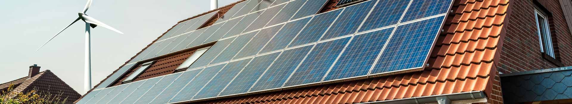 Solarmodule und Dachfenster auf einem Ziegeldach, dahinter ein Windrad