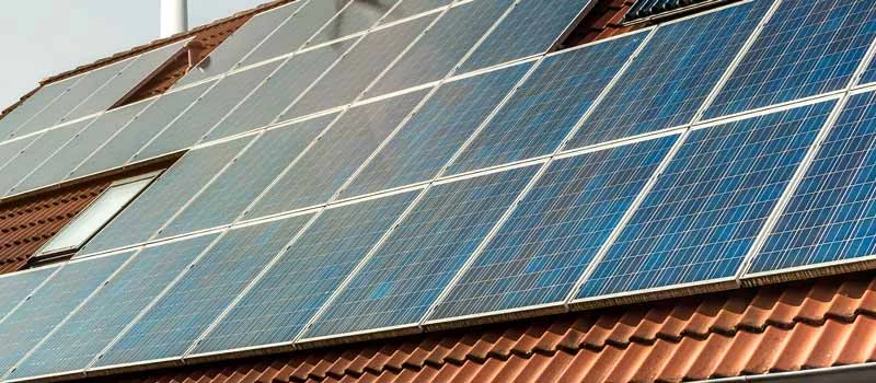Solarmodule und Dachfenster auf einem Ziegeldach, dahinter ein Windrad