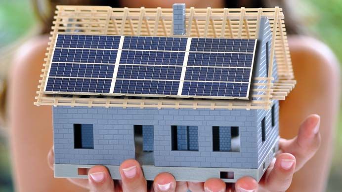 Hände halten ein kleines Hausmodell mit Solarmodulen auf dem Dach